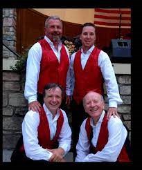A photo of the avalons standing posed in front of the Knoebels hawaiian bandshell in white shirts and red vests.