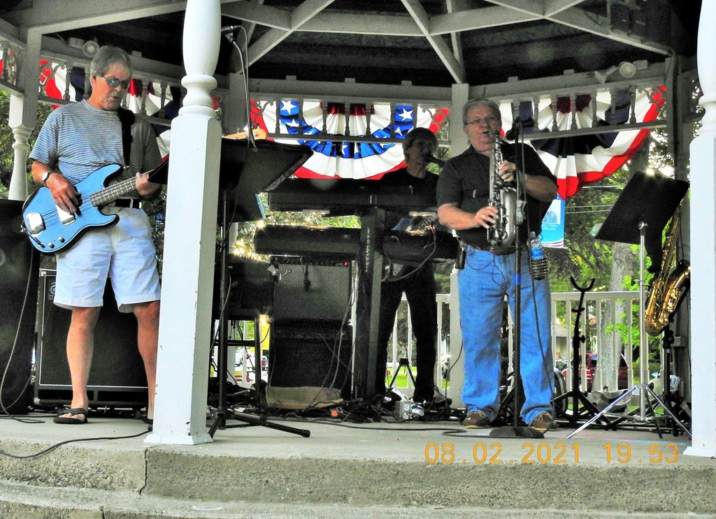 Photo of Memory Lane band members playing music inside of a gazebo. American flag colored banners hang off the gazebo in the background. 