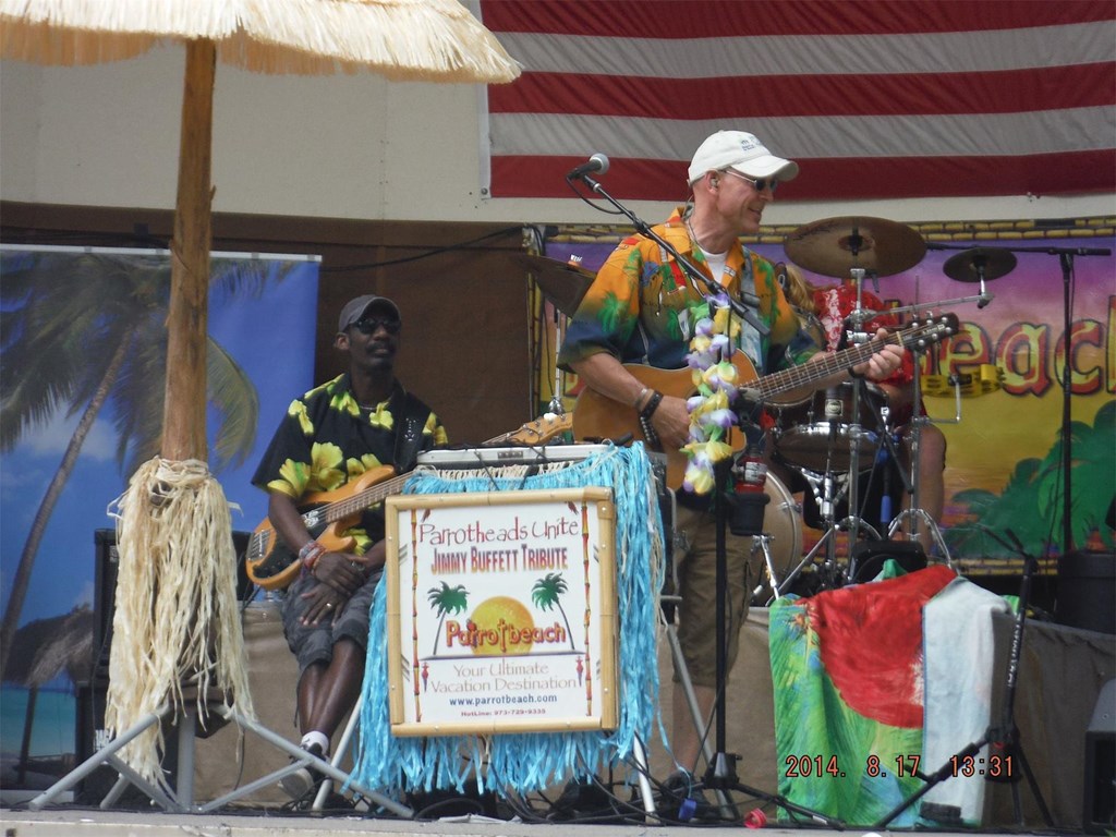 Two members of parrot beach stand performing on the Knoebels bandshell with their full island setup including palm umbrella and island backdrops. 