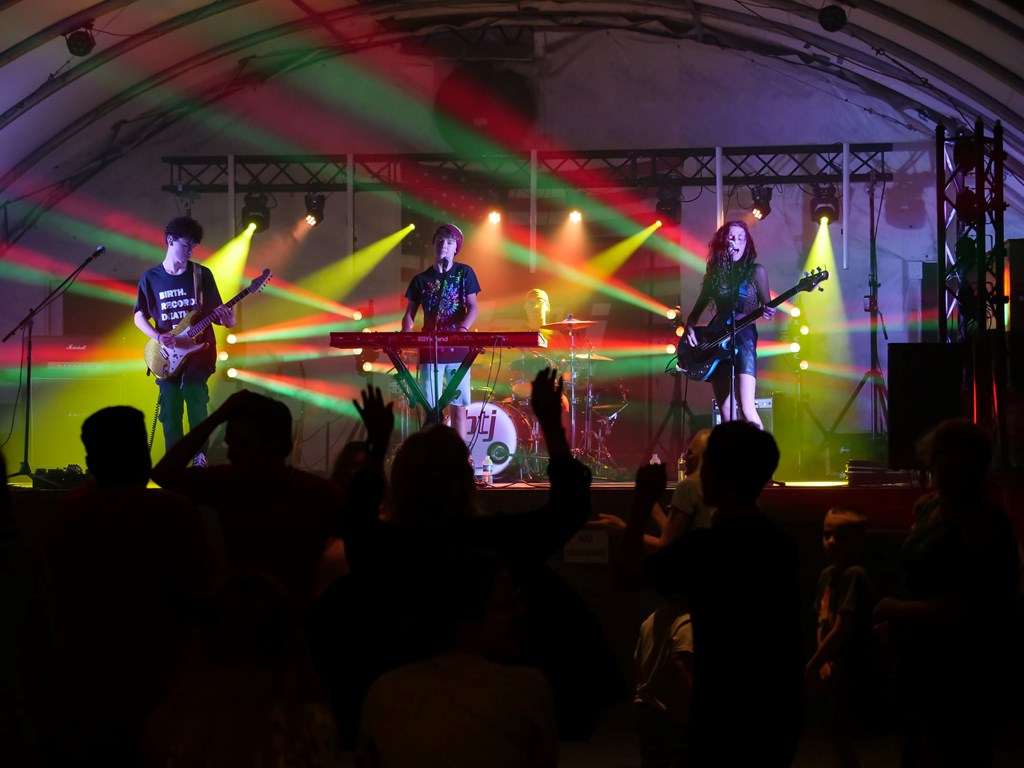 Photo of the four members of Burn the Jukebox on stage performing with a crowd of fans dancing below and an awesome red and green color themed light show behind them. 
